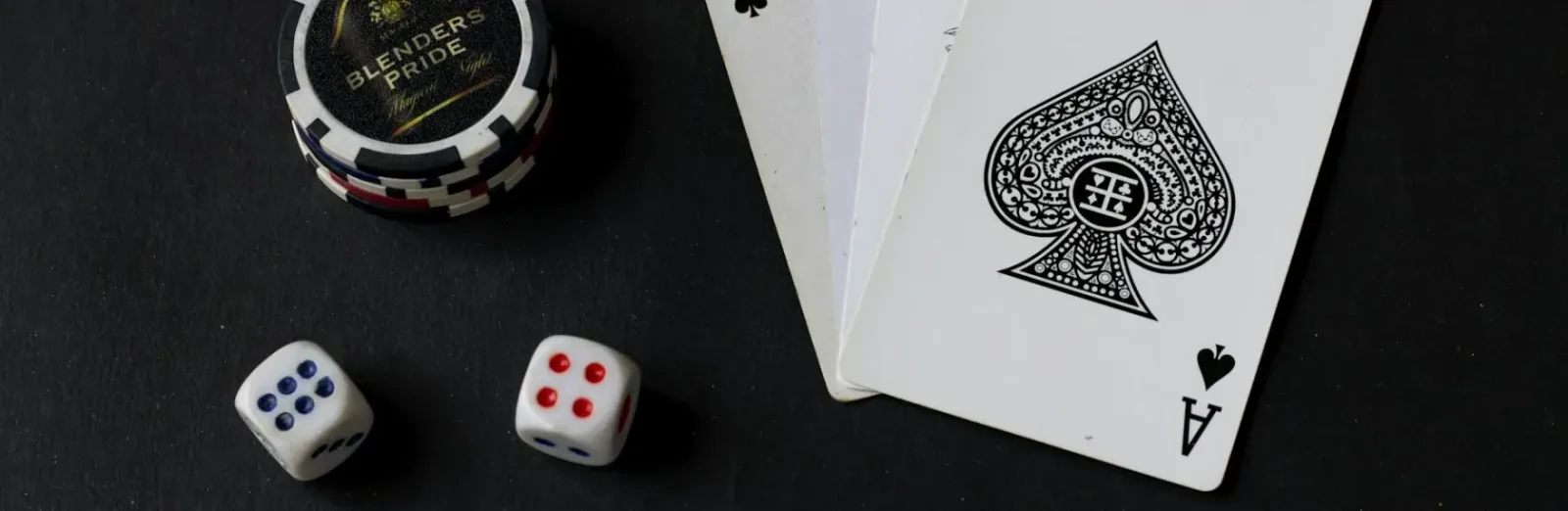 Fichas de casino apiladas junto a dos dados y una carta de as, sobre una mesa oscura.