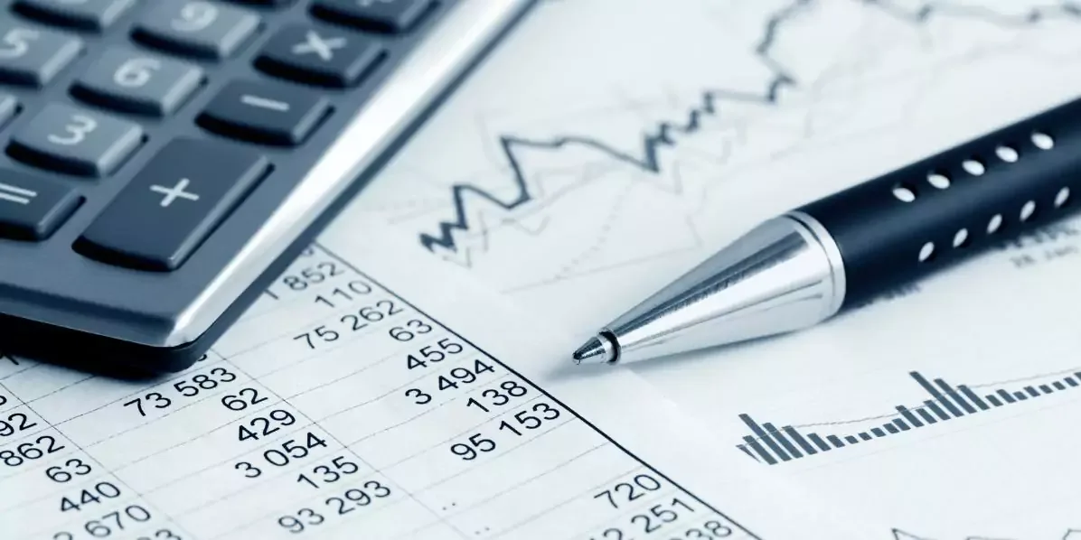 Calculadora y lapicero apoyados sobre hojas con columnas de números y un gráfico de barras.