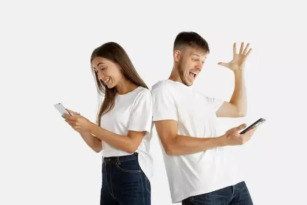Pareja joven de pie, espalda contra espalda, cada uno mirando la pantalla de su teléfono.